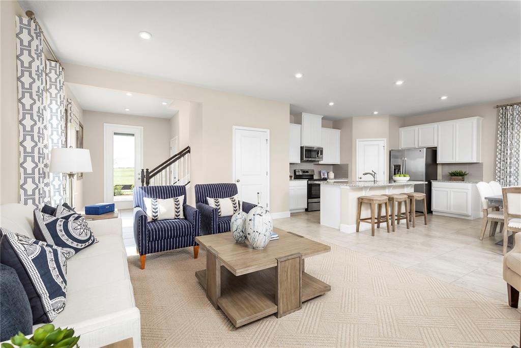 An open-concept living room and kitchen featuring white cabinetry, stainless steel appliances, and striped armchairs — 2441 WHITE LADYFISH ROAD, WIMAUMA, FL