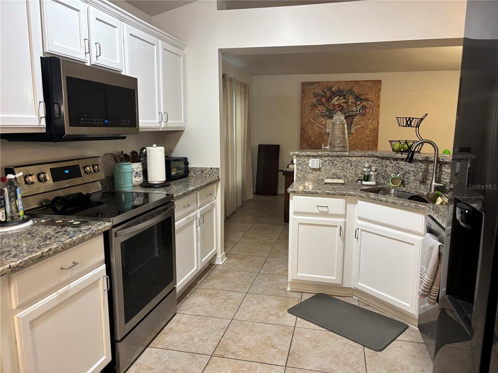 A kitchen with white cabinets, granite countertops, stainless steel appliances, and tile flooring — 304 MARION OAKS TRAIL, OCALA, FL
