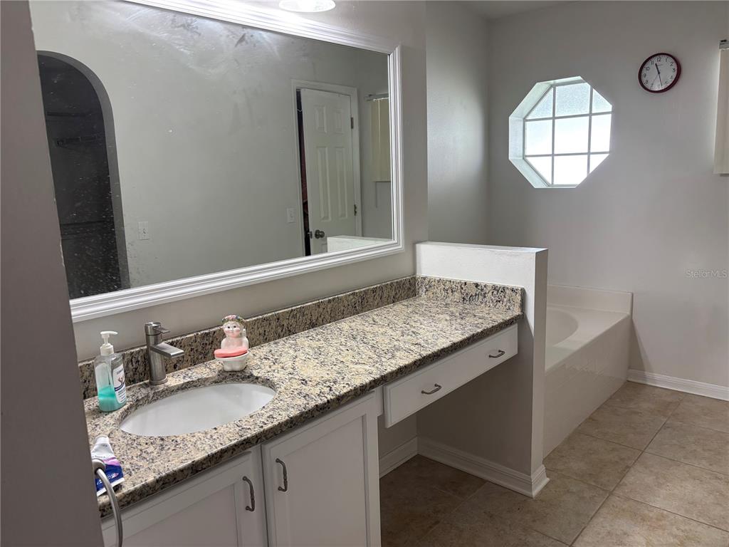 A bathroom features a granite vanity, white cabinets, a large mirror, and a soaking tub — 304 MARION OAKS TRAIL, OCALA, FL