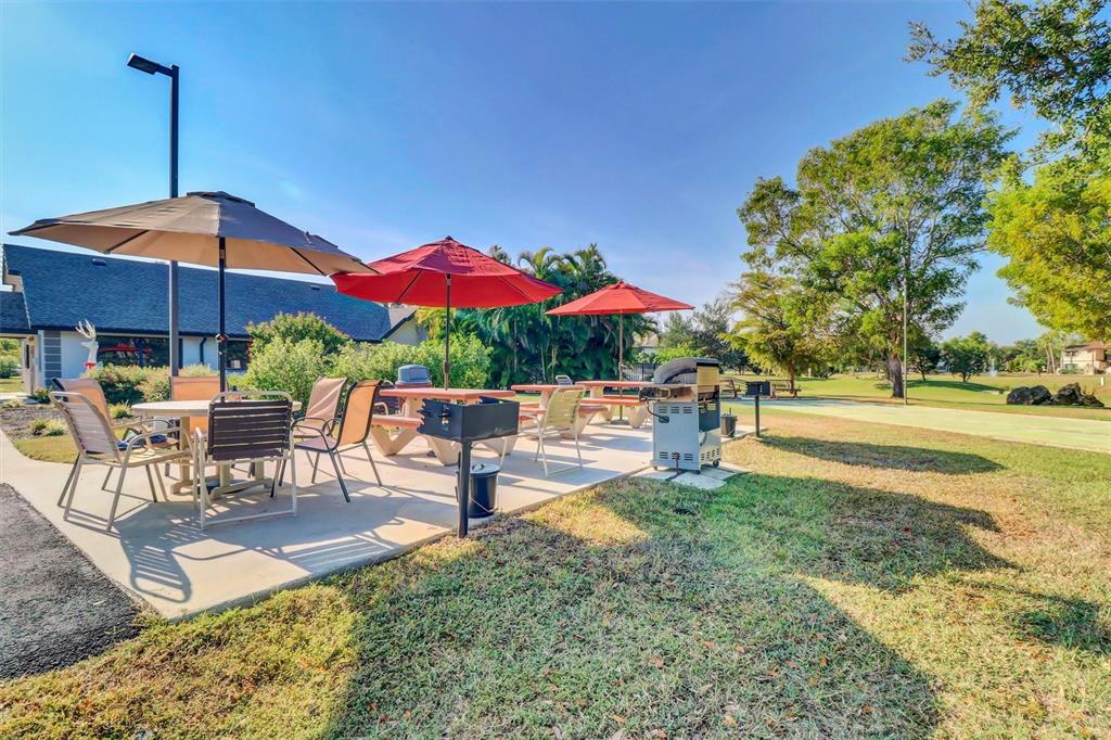 An outdoor patio area features picnic tables, umbrellas, and a grill on a concrete slab — 1515 FORREST NELSON BOULEVARD UNIT N104, PORT CHARLOTTE, FL