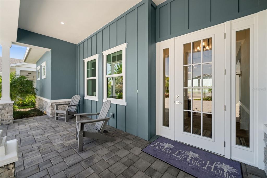 A covered front porch features blue board-and-batten siding, two gray chairs, and a glass-paneled door — 42231 LAKE TIMBER DRIVE, PUNTA GORDA, FL