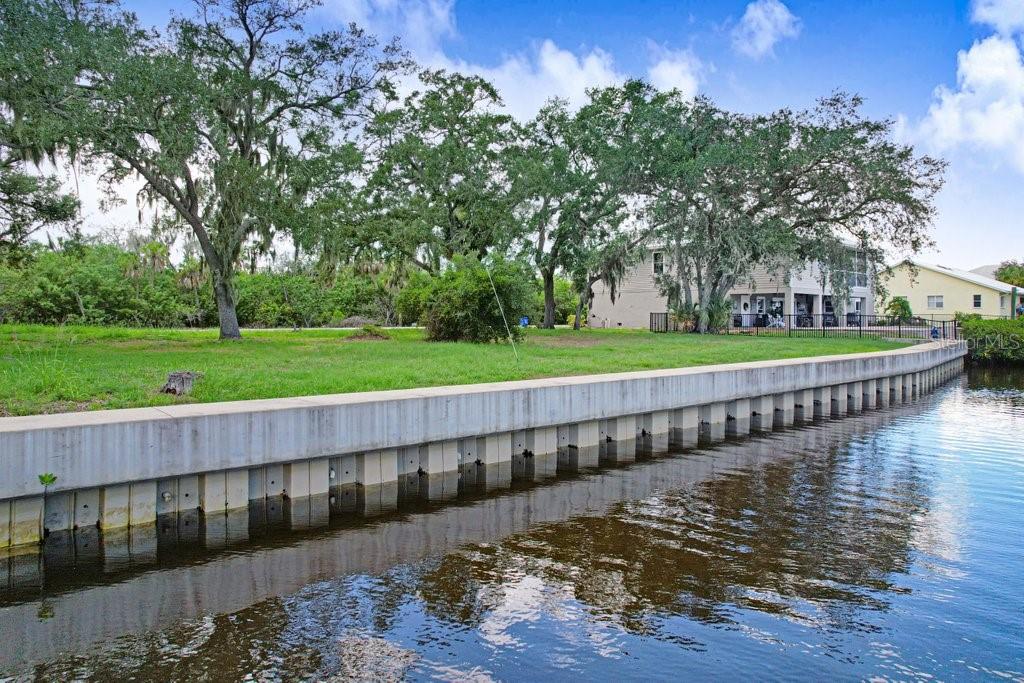 A concrete seawall borders a grassy lot with mature trees along a canal — 406 14TH STREET SW, RUSKIN, FL