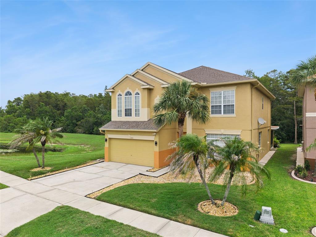 A two-story tan house with a two-car garage sits on a grassy lot with palms — 1860 WHITE HERON BAY CIRCLE, ORLANDO, FL