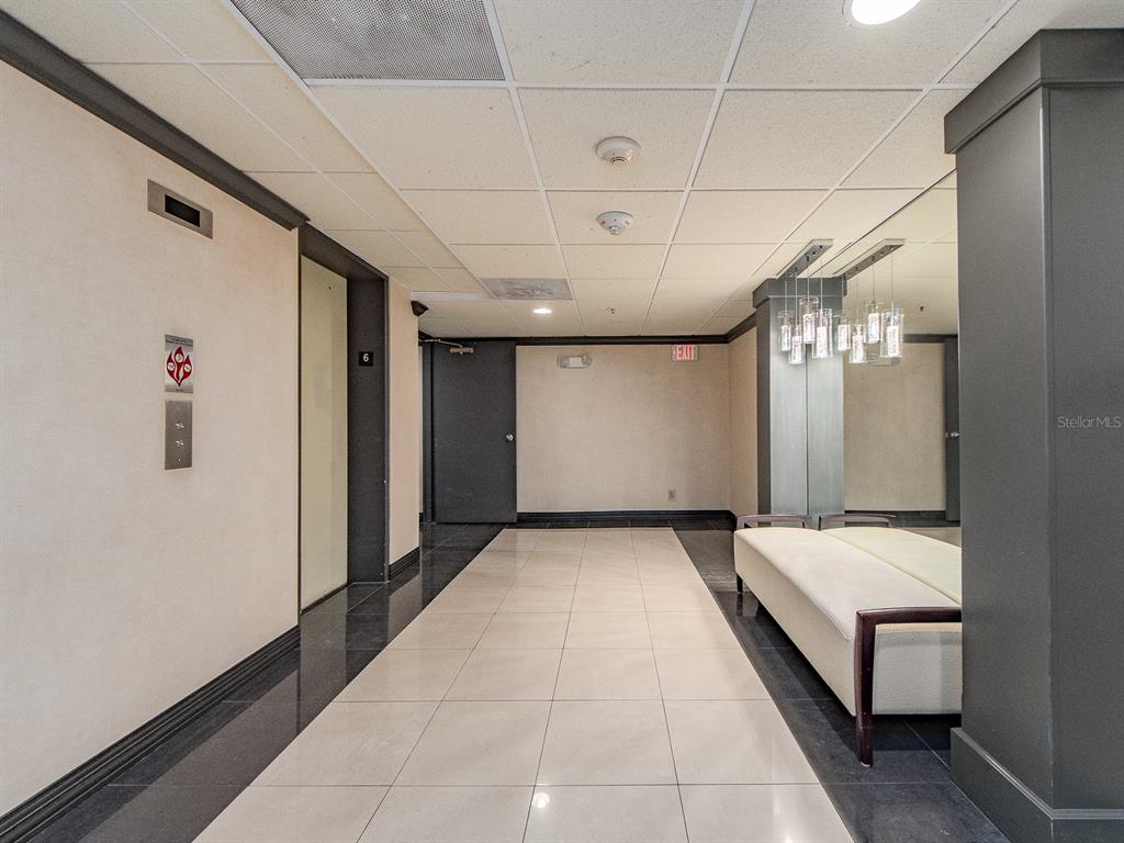 A modern elevator lobby features light tile flooring, a bench, and a mirrored wall — 1480 GULF BOULEVARD UNIT 612, CLEARWATER BEACH, FL