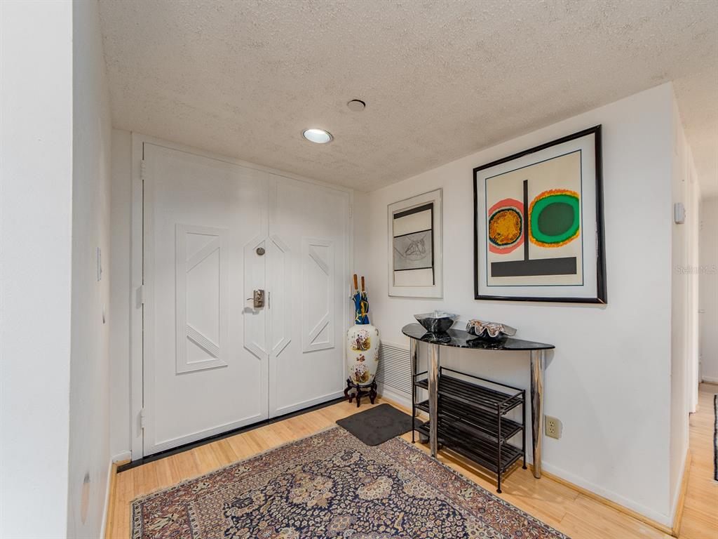 An entryway features a double door, a patterned rug, a console table, and wall art — 1480 GULF BOULEVARD UNIT 612, CLEARWATER BEACH, FL