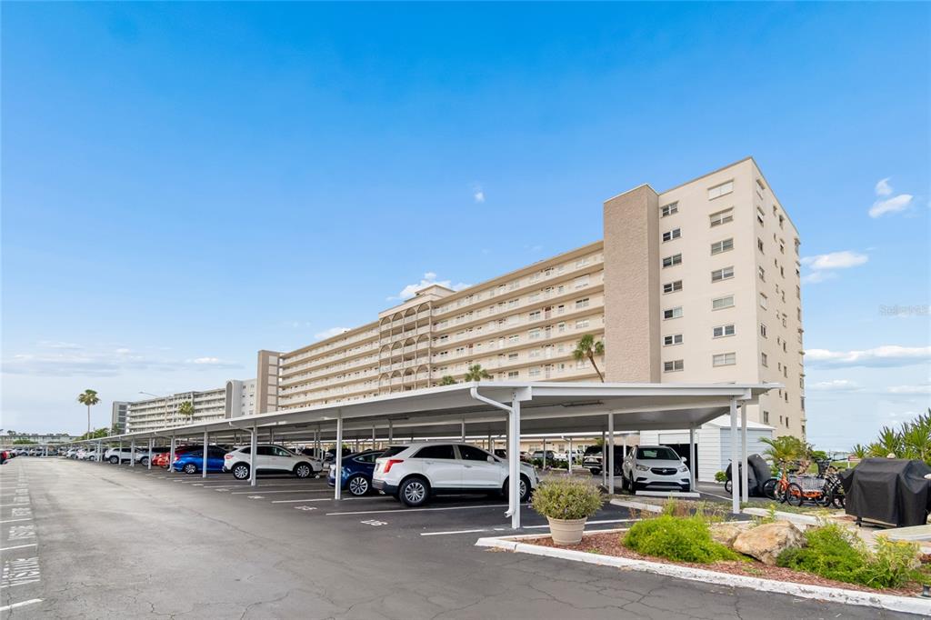 A multi-story apartment building features a large covered parking area with several parked cars — 5980 SHORE BOULEVARD S UNIT 909, GULFPORT, FL