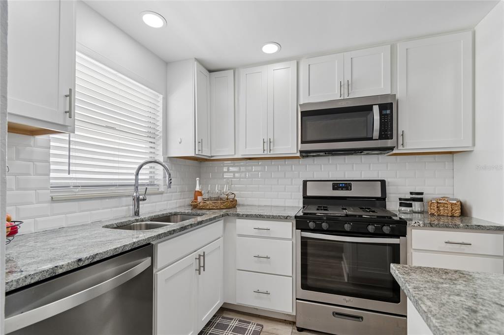 A kitchen with white cabinets, granite countertops, stainless steel appliances, and a subway tile backsplash — 5980 SHORE BOULEVARD S UNIT 909, GULFPORT, FL