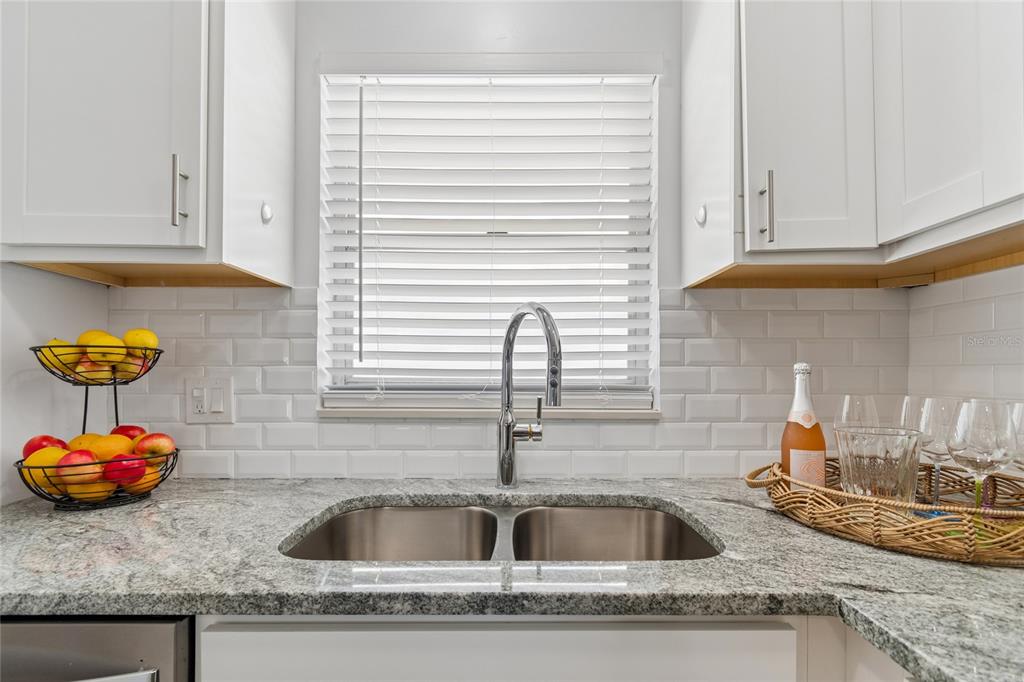 A kitchen sink area features white cabinets, subway tile backsplash, and granite countertops — 5980 SHORE BOULEVARD S UNIT 909, GULFPORT, FL