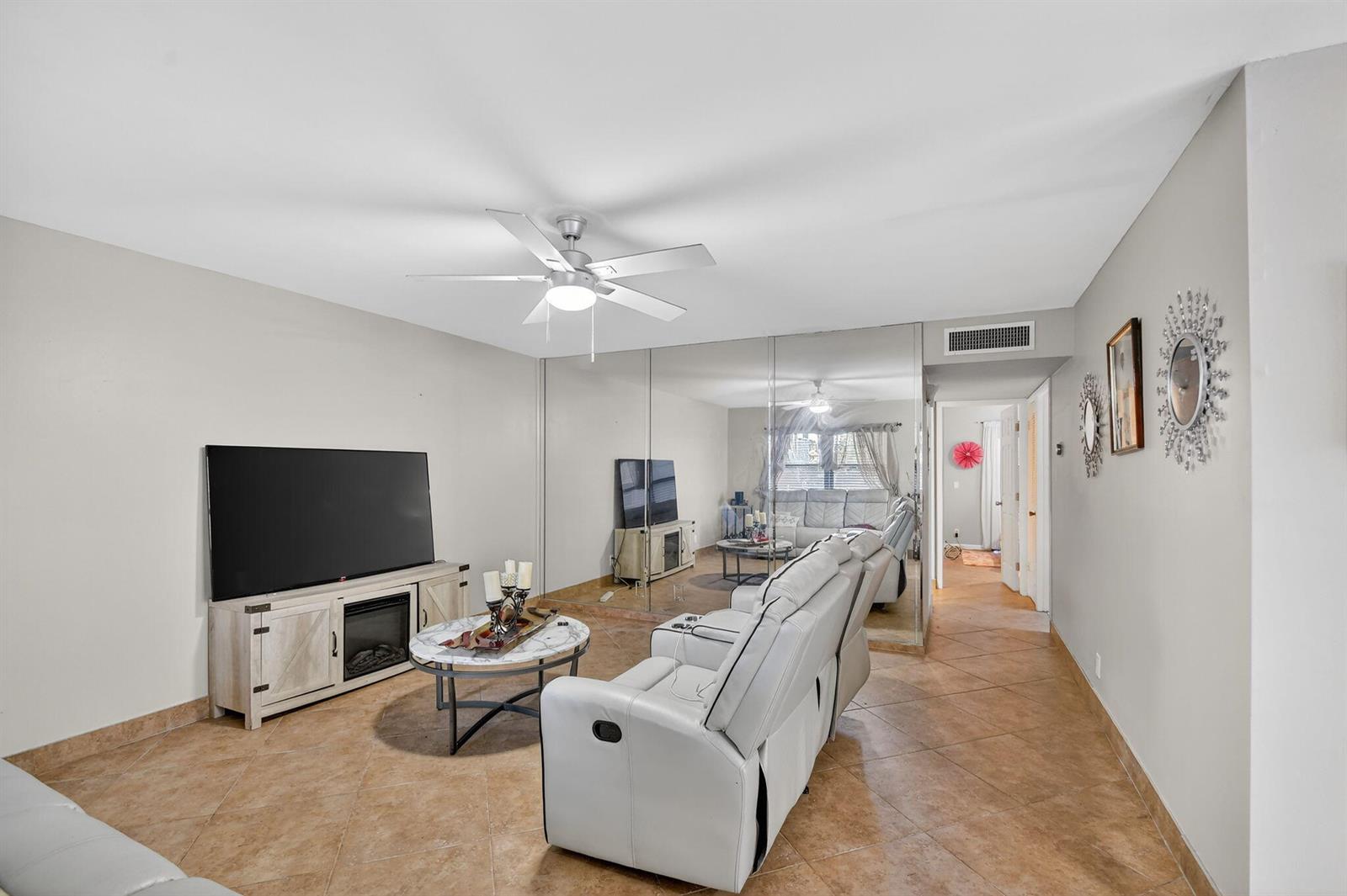 A living room features a television, white reclining sofa, marble coffee table, and mirrored wall — 743 Burgundy P, Delray Beach FL 33484, DELRAY BEACH, FL