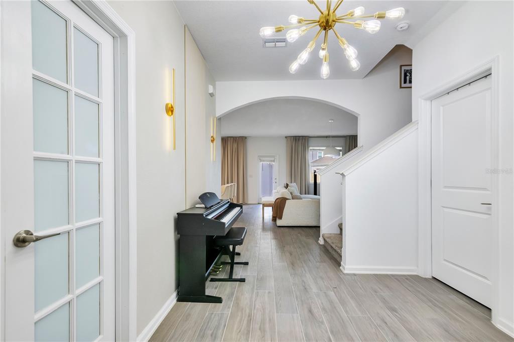 A foyer features wood-look tile flooring, a black digital piano, and a modern gold chandelier — 2865 FITNESS ST, CLERMONT, FL