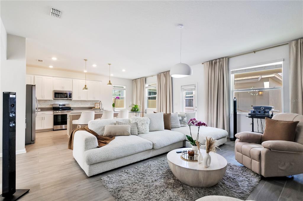 An open-concept living room and kitchen featuring white cabinetry, a large sectional, and light flooring — 2865 FITNESS ST, CLERMONT, FL