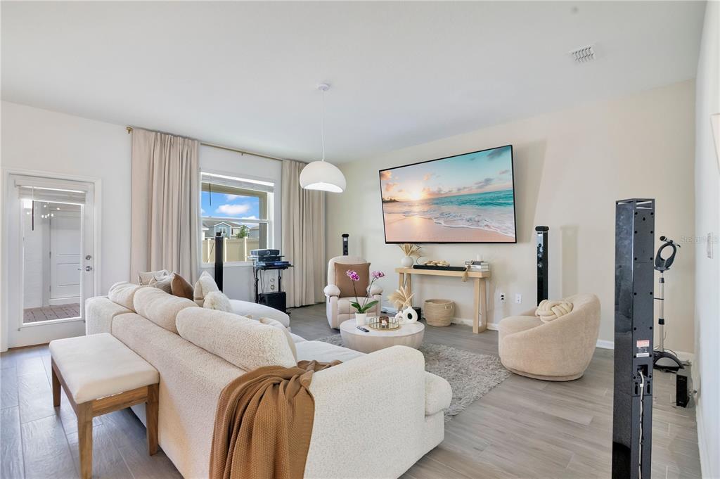 A living room features a large television, light-colored furniture, and wood-look tile flooring — 2865 FITNESS ST, CLERMONT, FL