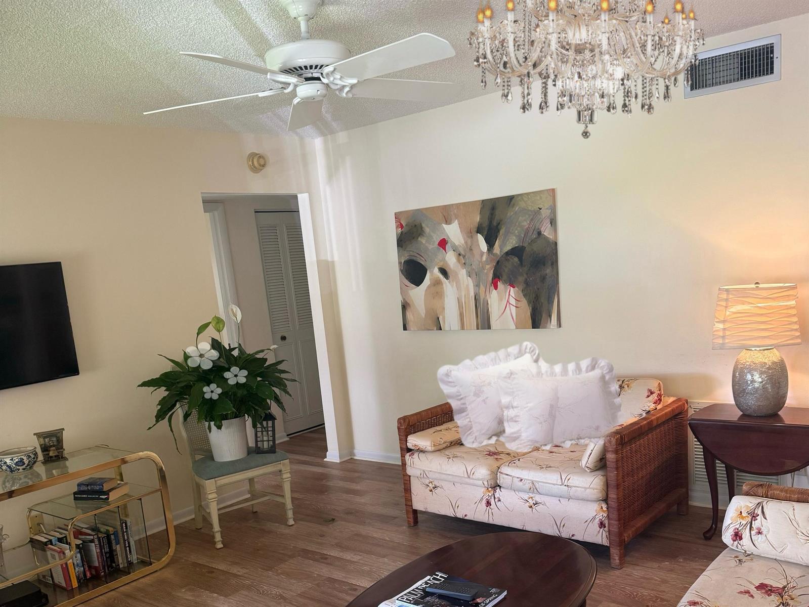 A living room features a wicker loveseat, a crystal chandelier, a ceiling fan, and artwork — 519 Shady Pine Way # A2, FL 33415, FL