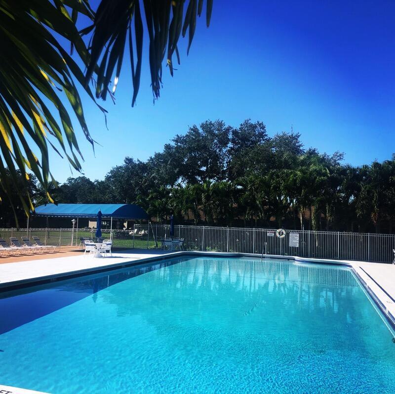 A rectangular outdoor swimming pool is surrounded by a white fence and palm trees — 519 Shady Pine Way # A2, FL 33415, FL