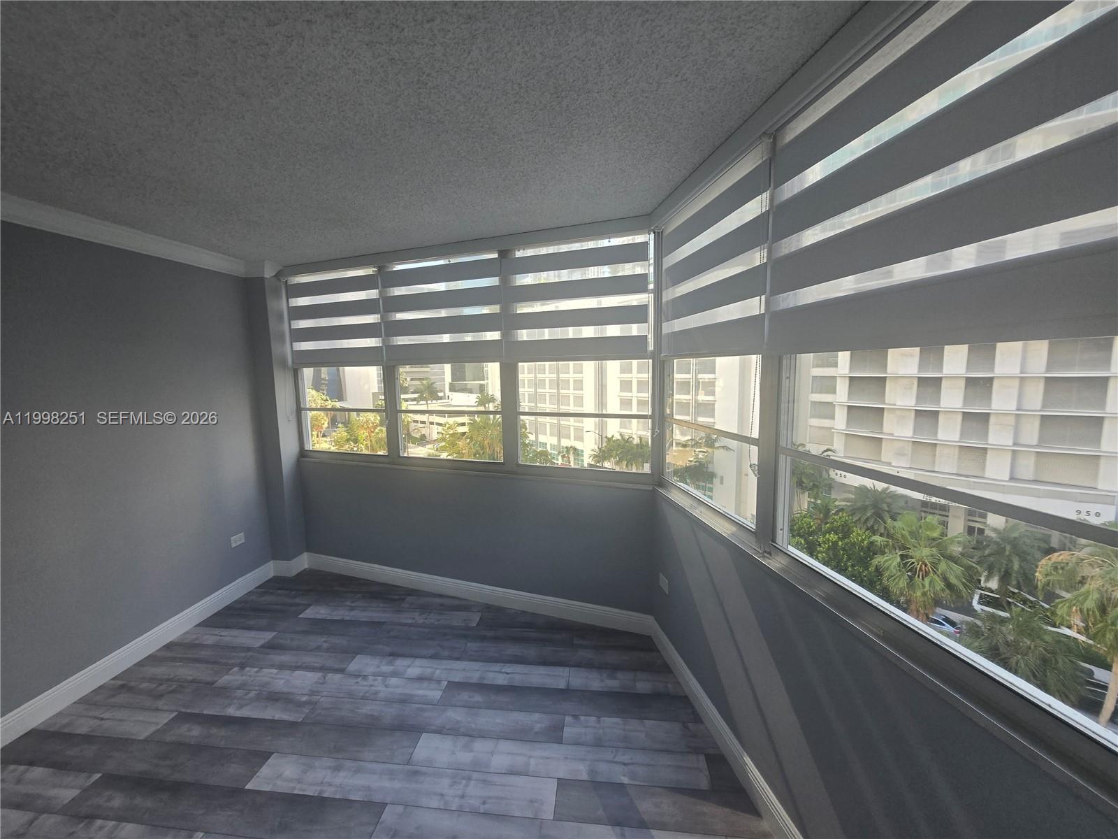 An empty room features gray walls, wood-look flooring, and large windows with striped roller shades — 825 Brickell Bay Dr # 750, Miami FL 33131, MIAMI, FL