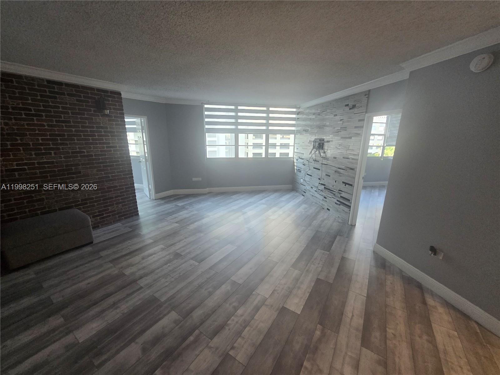 An empty living room features wood-look flooring, a brick accent wall, and a stone-tiled wall — 825 Brickell Bay Dr # 750, Miami FL 33131, MIAMI, FL