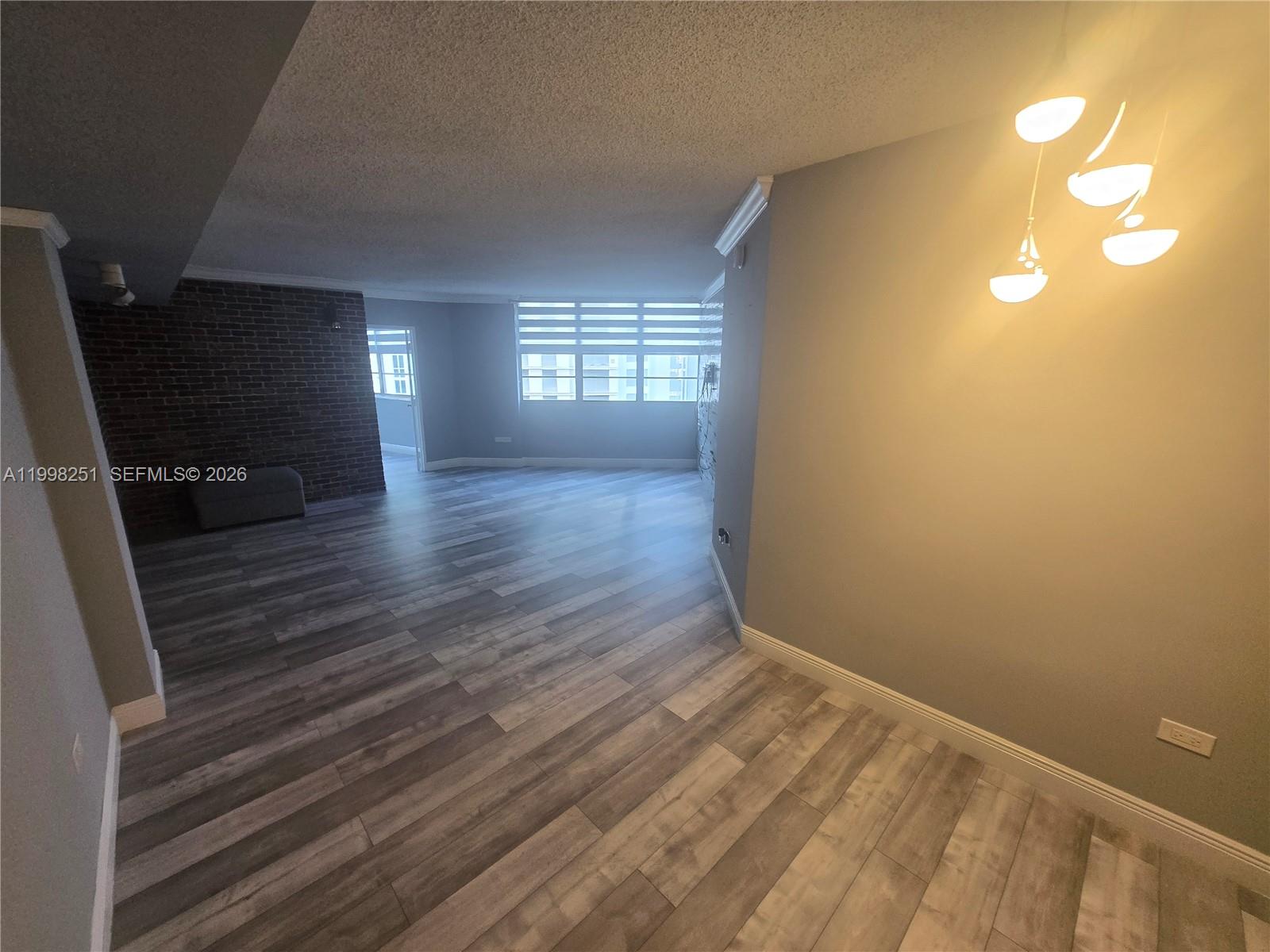 An open-concept living area features wood-look flooring, a brick accent wall, and modern lighting — 825 Brickell Bay Dr # 750, Miami FL 33131, MIAMI, FL