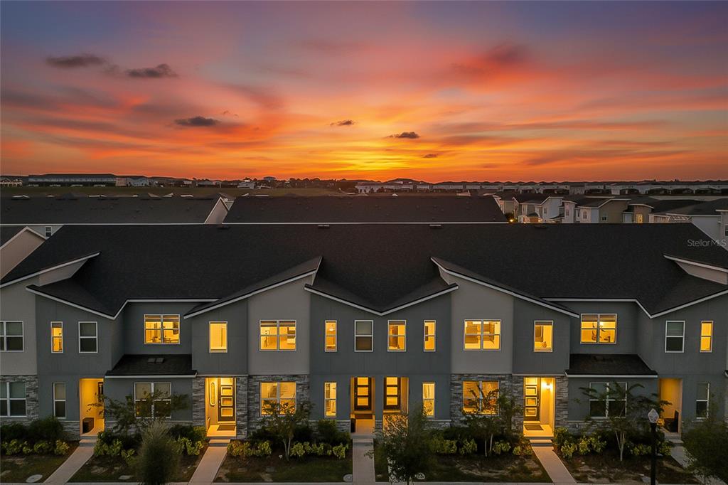 An exterior view of a multi-unit townhouse complex at sunset with a dramatic orange sky — 2382 ZABALLINA PLACE, KISSIMMEE, FL