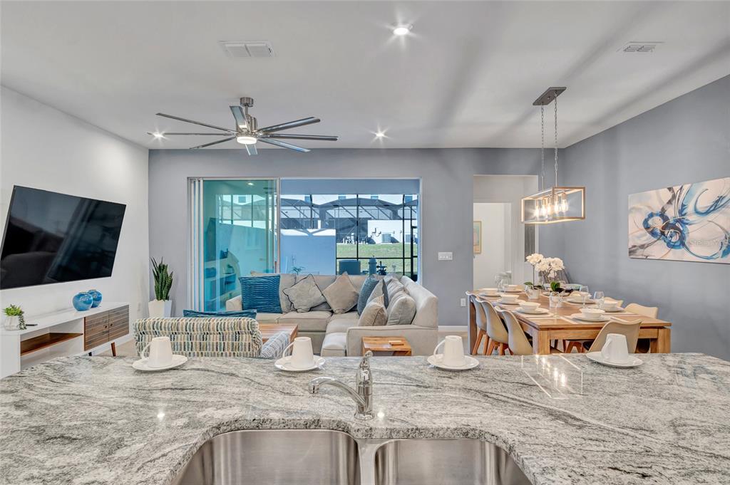 A kitchen island with a granite countertop overlooks a living room and dining area — 2382 ZABALLINA PLACE, KISSIMMEE, FL