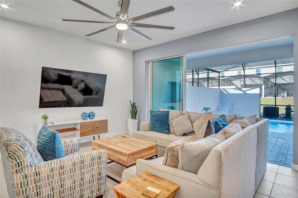 A living room features a sectional sofa, patterned armchair, television, and sliding doors to a pool — 2382 ZABALLINA PLACE, KISSIMMEE, FL