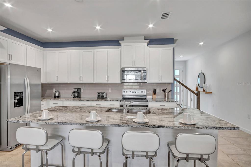 A kitchen features white cabinets, a granite island with four stools, and stainless steel appliances — 2382 ZABALLINA PLACE, KISSIMMEE, FL