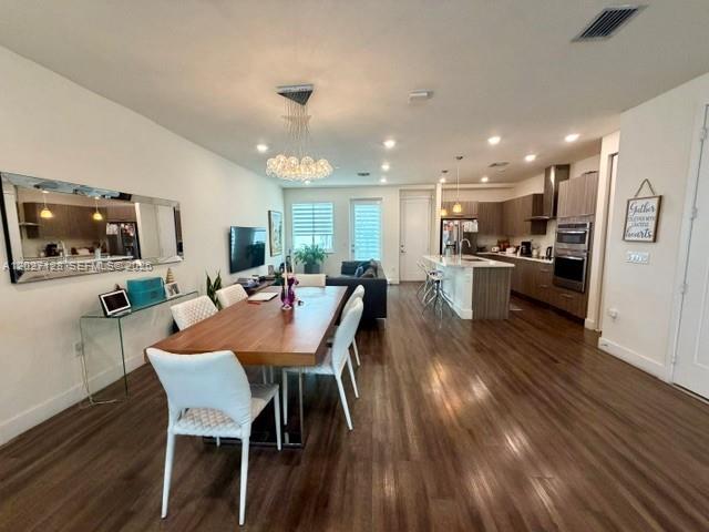 An open-concept dining area features a wooden table, modern chandelier, and adjacent kitchen — DORAL, FL