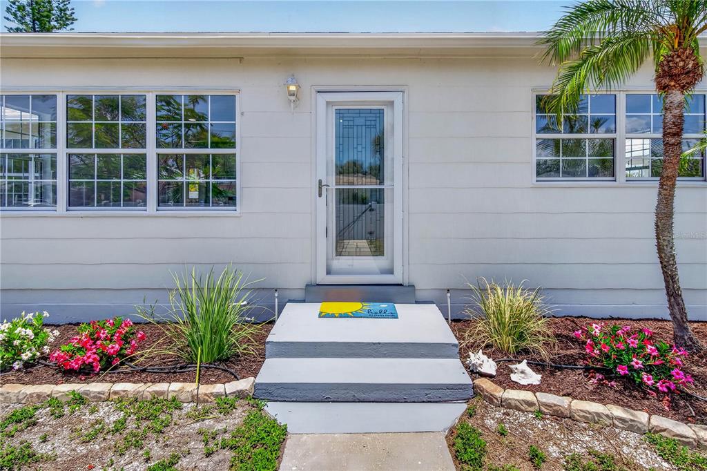 A white house exterior features a front door with a storm door and concrete steps — 260 42ND AVENUE, ST PETE BEACH, FL