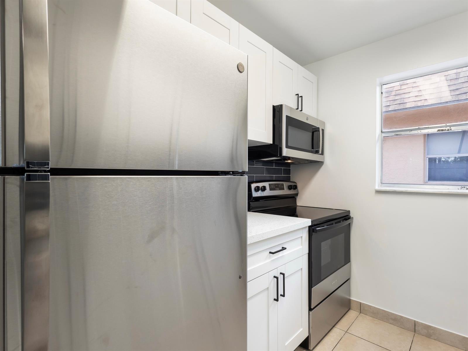 A kitchen features stainless steel appliances, white cabinets, a black backsplash, and a window — 450 SW 2nd Avenue # 2050, Boca Raton FL 33432, BOCA RATON, FL
