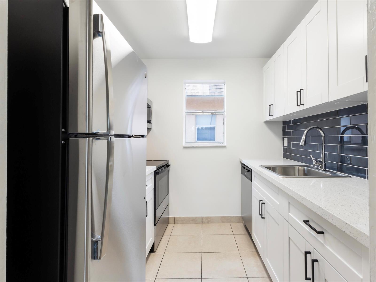A galley kitchen features white cabinets, stainless steel appliances, a dark tile backsplash, and tile flooring — 450 SW 2nd Avenue # 2050, Boca Raton FL 33432, BOCA RATON, FL