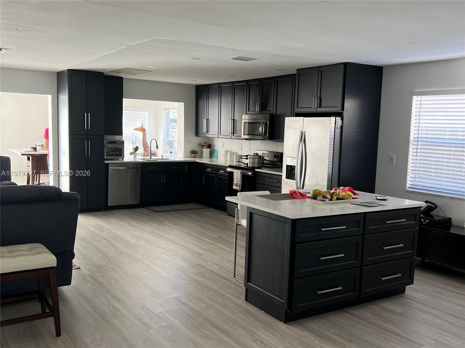 A modern kitchen features dark cabinetry, white countertops, stainless steel appliances, and light wood flooring — 3771 NE 16th Ave, Pompano Beach FL 33064, POMPANO BEACH, FL