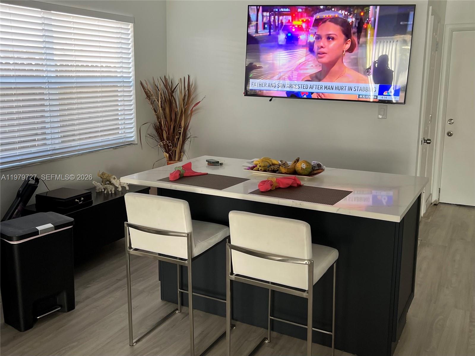 A kitchen island with two white stools sits in a room with a wall-mounted television — 3771 NE 16th Ave, Pompano Beach FL 33064, POMPANO BEACH, FL