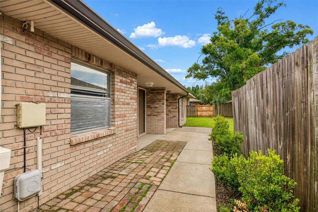 A brick house exterior features a paved walkway, a wooden fence, and a small yard — 3132 BLOOMINGDALE VILLAS COURT, BRANDON, FL