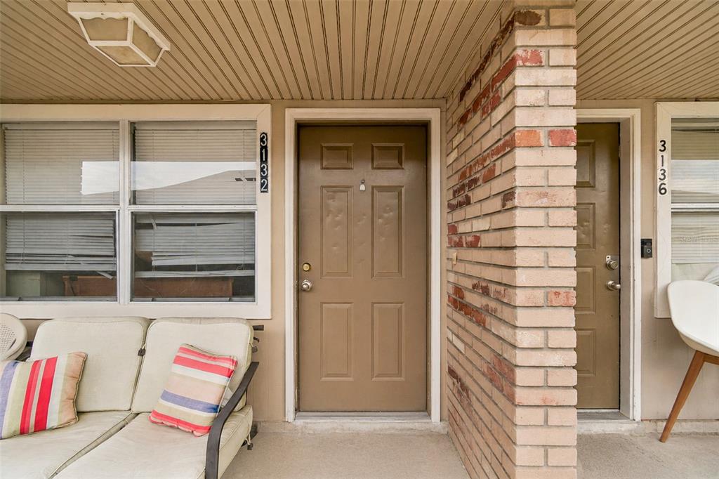 A covered porch features two brown entry doors, a brick pillar, and outdoor seating — 3132 BLOOMINGDALE VILLAS COURT, BRANDON, FL