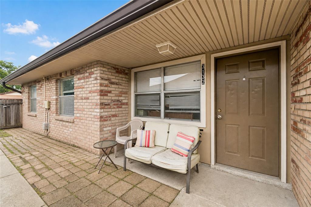 A brick exterior home features a paved patio, a brown front door, and outdoor seating — 3132 BLOOMINGDALE VILLAS COURT, BRANDON, FL
