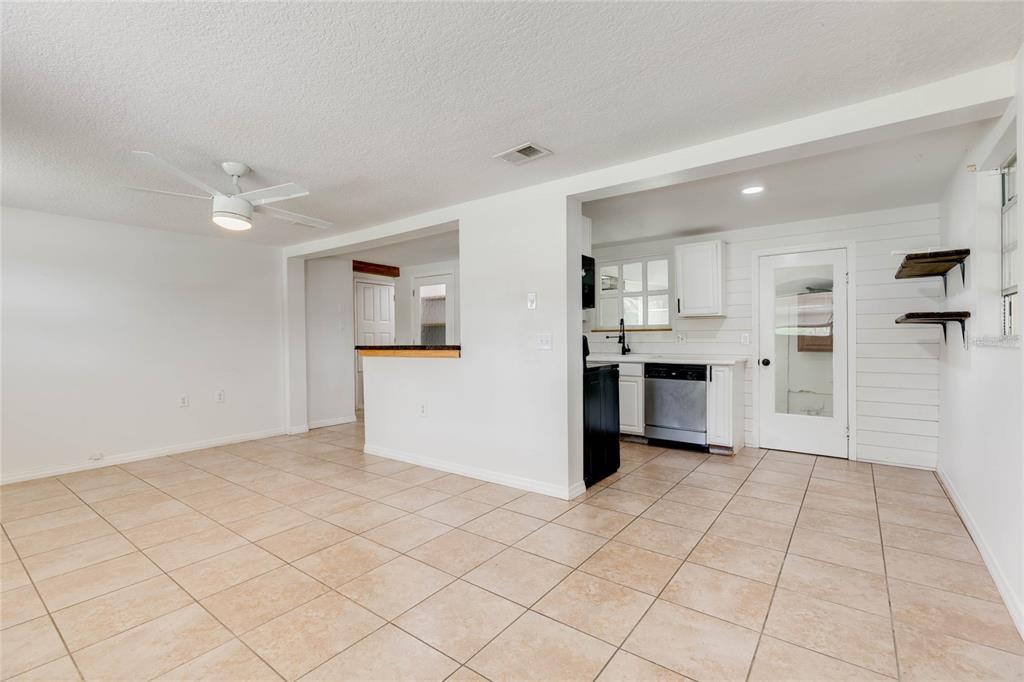 A bright room with beige tile flooring, a ceiling fan, and an open kitchen area — 4181 CHESTNUT DRIVE, MOUNT DORA, FL
