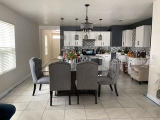 A dining area with a glass table and gray chairs sits before an open kitchen — 3547 FORSTER AVENUE, LEESBURG, FL