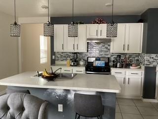 A kitchen features white cabinets, a central island with a sink, and three pendant lights — 3547 FORSTER AVENUE, LEESBURG, FL