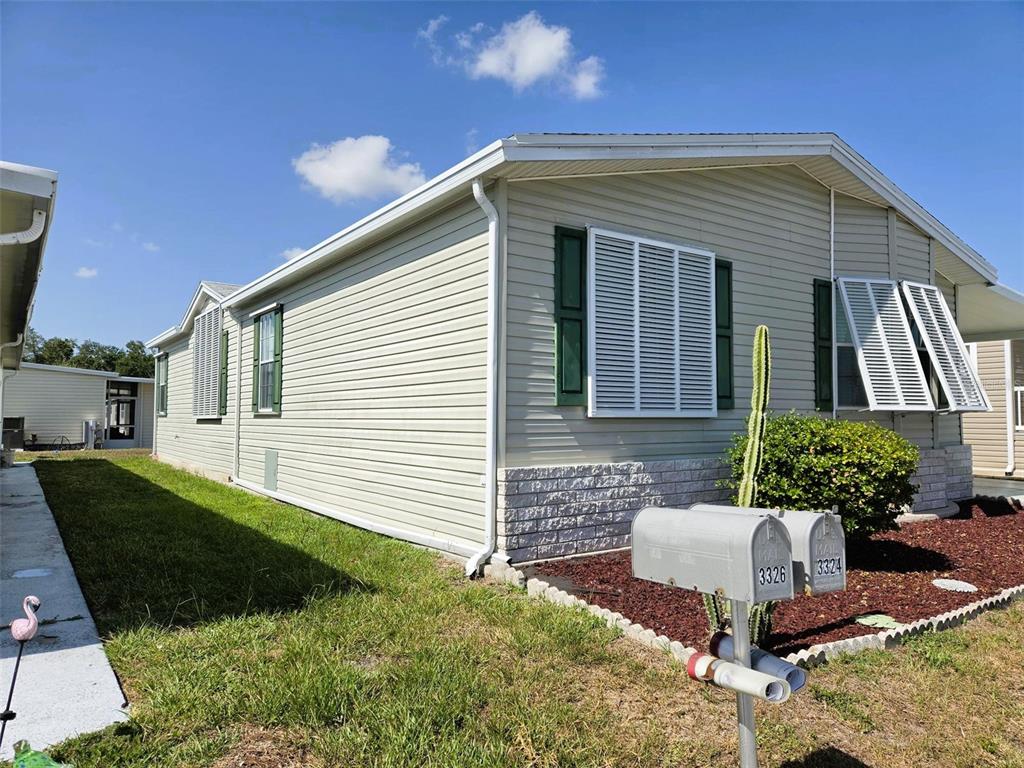 A light-colored mobile home exterior features green shutters, a stone-textured base, and two mailboxes — 3324 OVERCUP OAK TERRACE, SARASOTA, FL