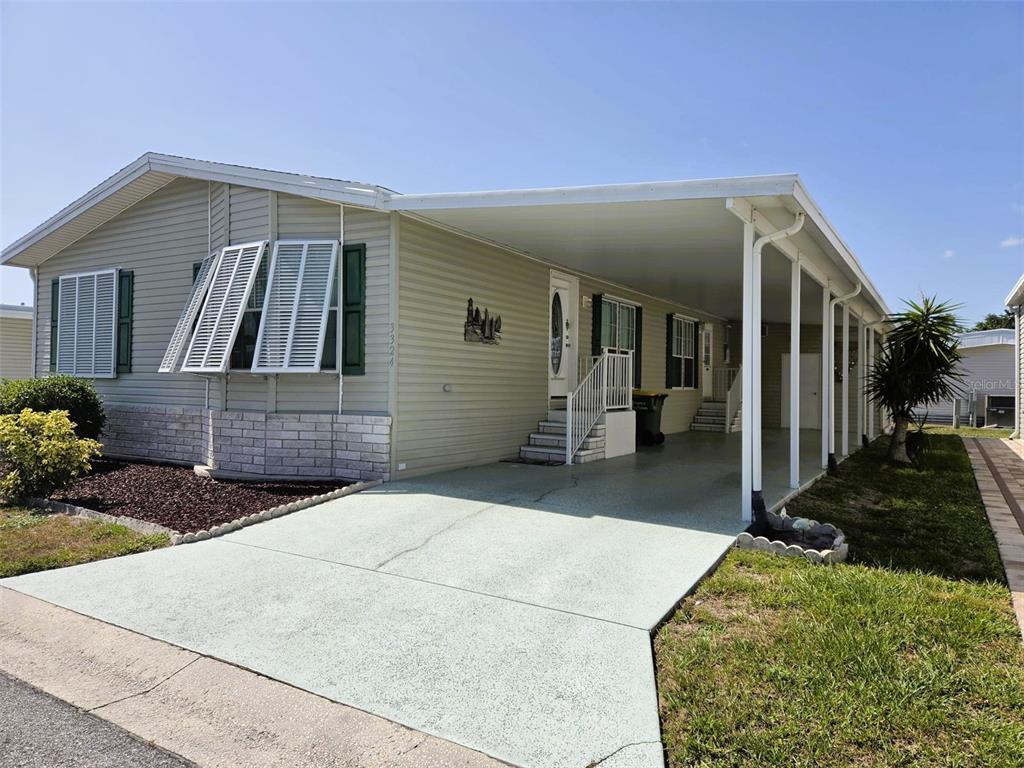 A light-colored manufactured home features a carport, stone skirting, and shutters on the front windows — 3324 OVERCUP OAK TERRACE, SARASOTA, FL