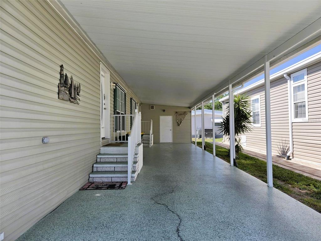 A covered carport with a speckled concrete floor leads to a home entrance with stairs — 3324 OVERCUP OAK TERRACE, SARASOTA, FL