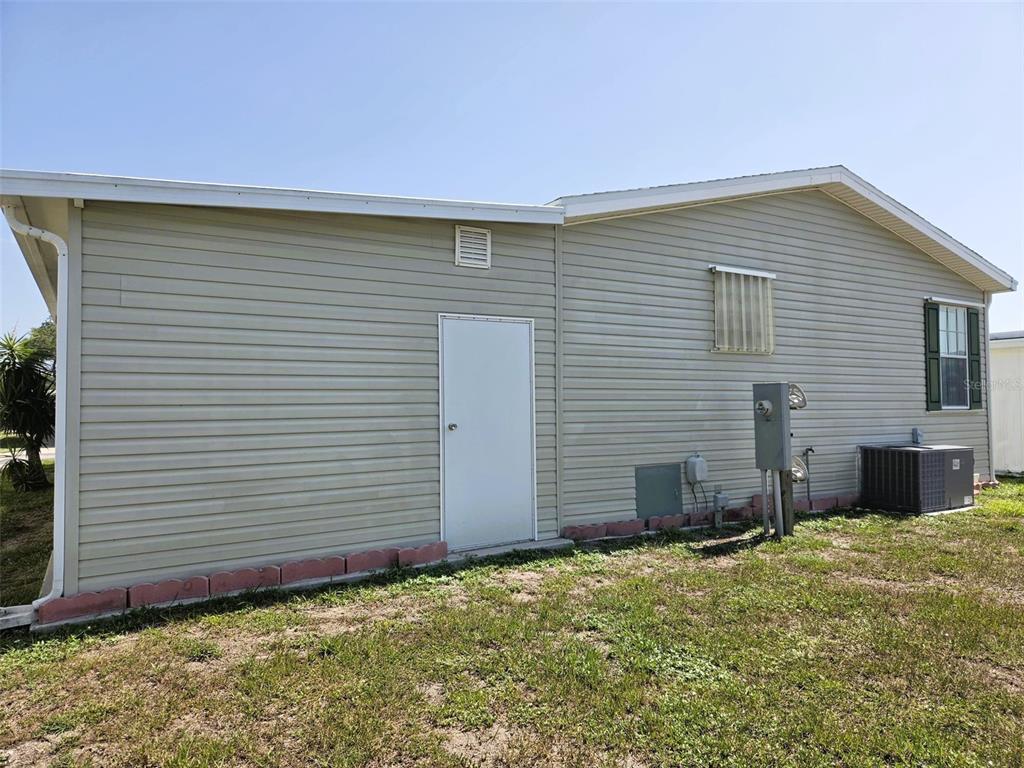 The exterior side of a light-colored vinyl-sided house features a white door and HVAC unit — 3324 OVERCUP OAK TERRACE, SARASOTA, FL