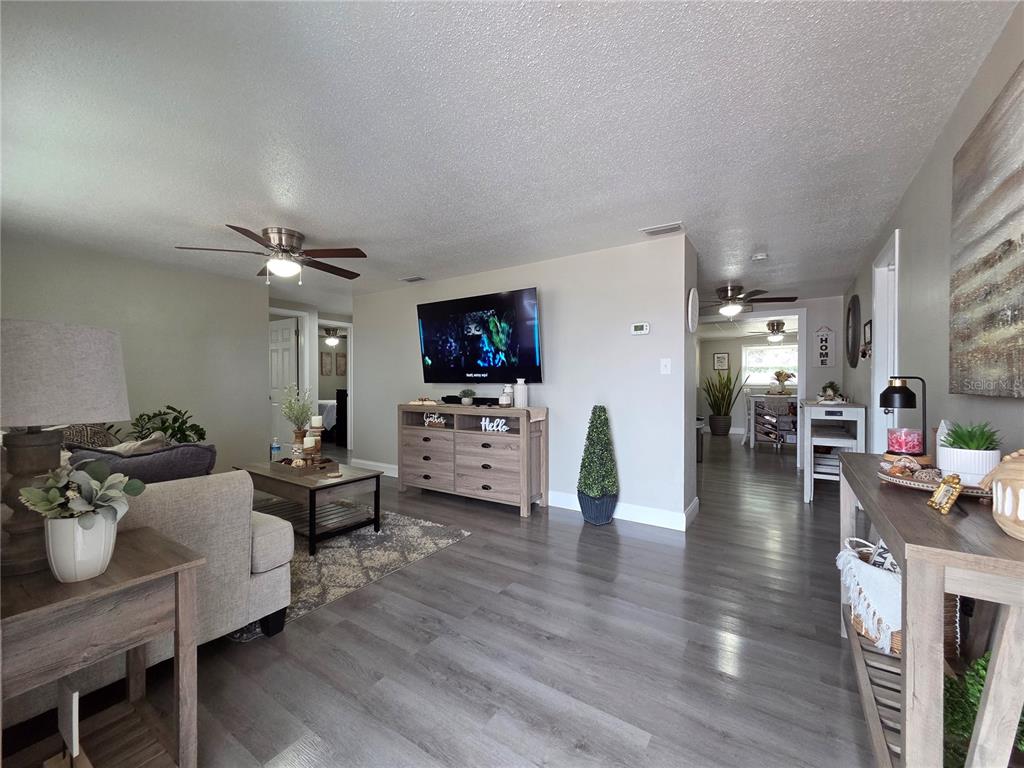 A living room features gray wood-look flooring, a wall-mounted television, and an open floor plan — 4834 GASLIGHT AVENUE, HOLIDAY, FL