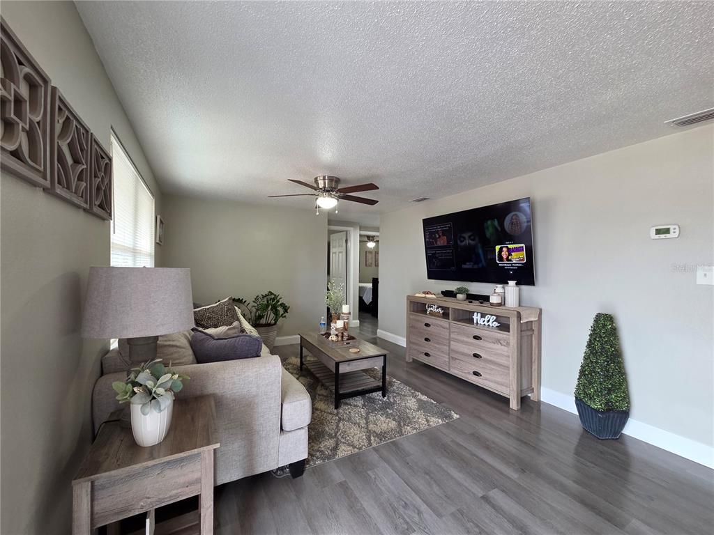 A living room features gray wood-look flooring, a sofa, a coffee table, and a television — 4834 GASLIGHT AVENUE, HOLIDAY, FL