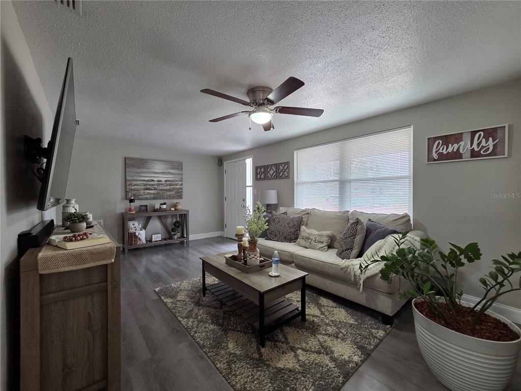 A living room features gray wood-look flooring, a beige sofa, and a ceiling fan — 4834 GASLIGHT AVENUE, HOLIDAY, FL