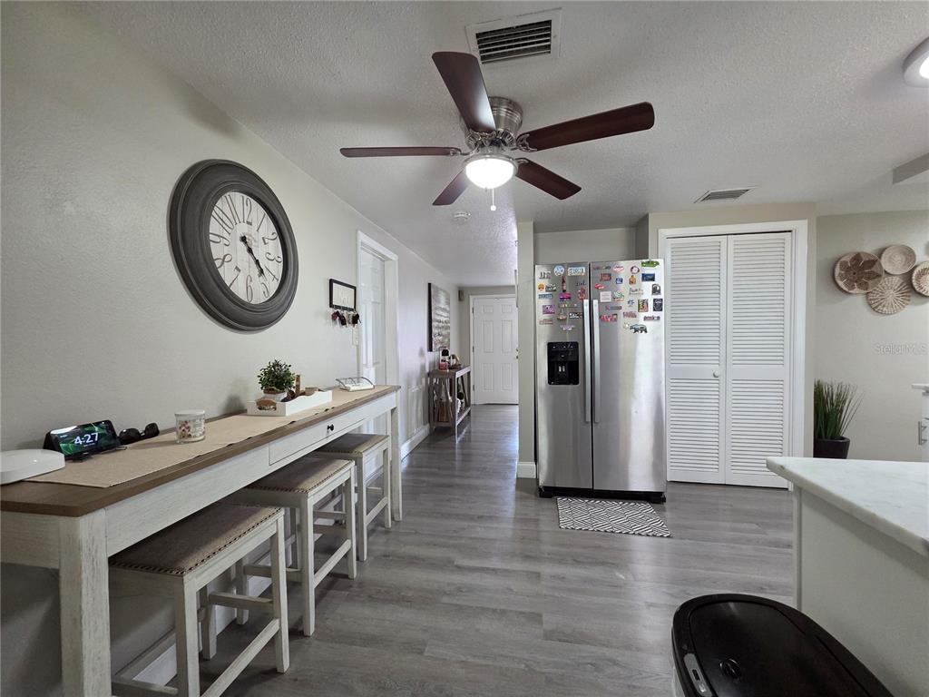 A kitchen area features a long console table with stools, a refrigerator, and wood-look flooring — 4834 GASLIGHT AVENUE, HOLIDAY, FL