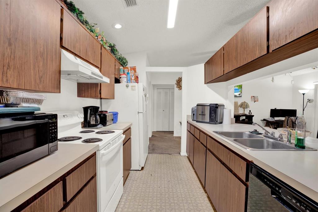 A galley kitchen features wood cabinets, white appliances, and a double-basin sink — 7502 GADSDEN DRIVE, TEMPLE TERRACE, FL