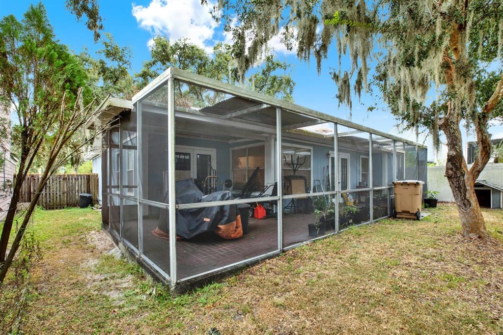 A screened-in patio with a brick floor sits behind a house under large oak trees — 7502 GADSDEN DRIVE, TEMPLE TERRACE, FL
