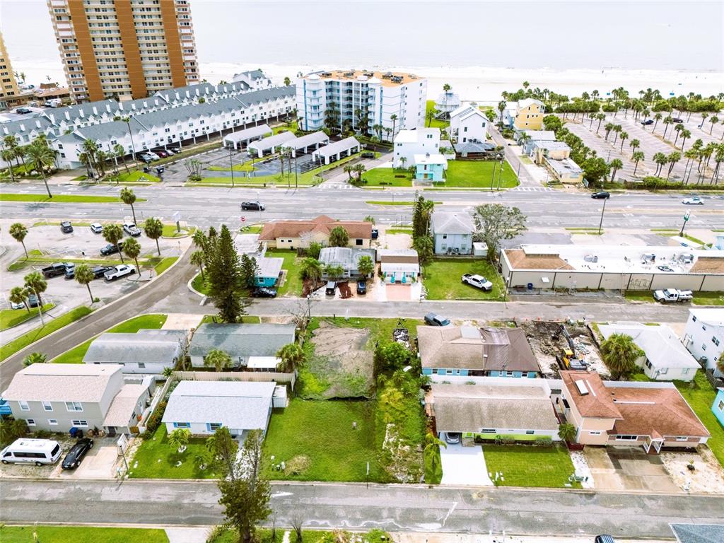 An aerial view shows a coastal neighborhood with residential houses, parking lots, and nearby hotels — 18005 1ST STREET E, ST PETERSBURG, FL