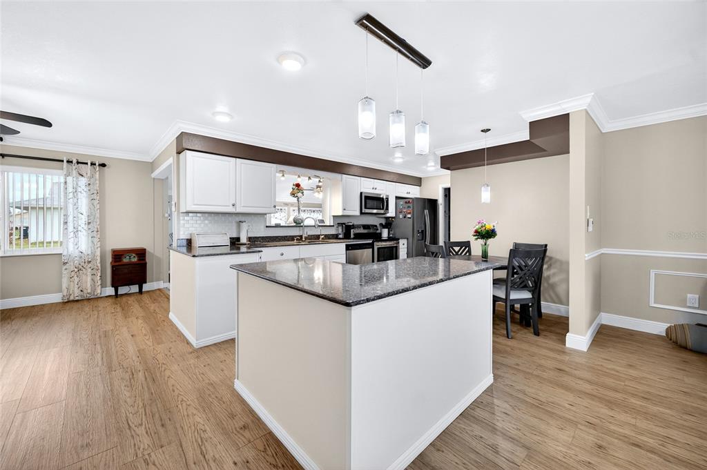 A kitchen with white cabinets, a granite-topped island, and light wood-look flooring — 1743 COUNCIL DRIVE, SUN CITY CENTER, FL