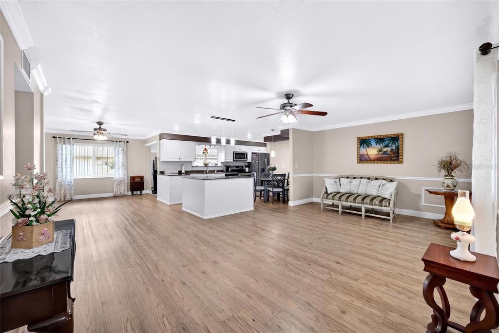 An open-concept living area features light wood-look flooring, a white kitchen island, and a dining space — 1743 COUNCIL DRIVE, SUN CITY CENTER, FL